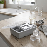 Forma de silicone em use na cozinha com cubos de gelo prontos ao lado de bebida
