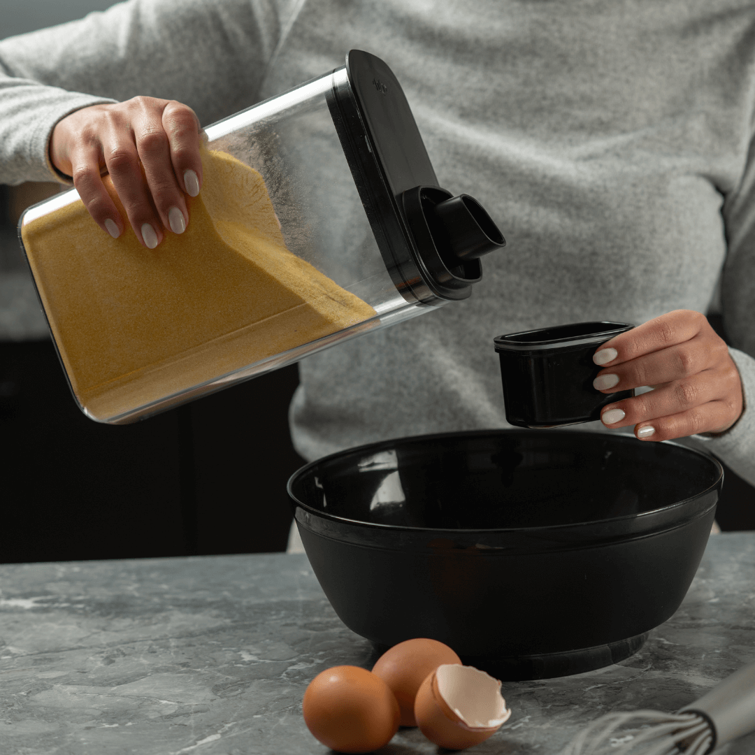 mulher despejando farinha do pote com medidor em tigela preta na cozinha