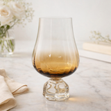 taca para vinho com degradê ambar sobre mesa de marmore e flores brancas ao fundo