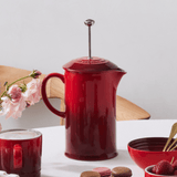 Cafeteira com mexedor, alça e tampa vermelha na mesa posta de café da manhã