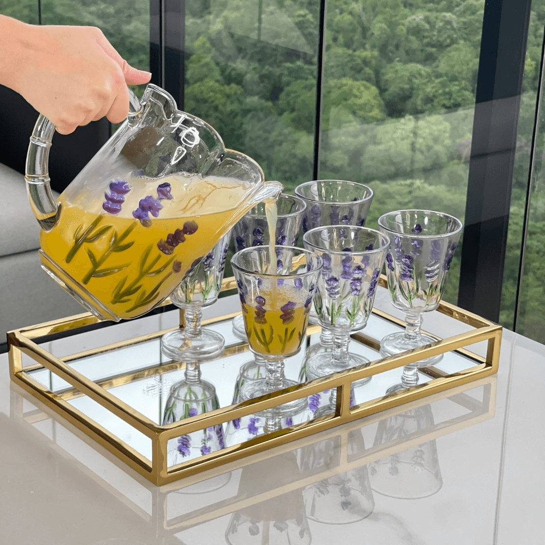 Jarra e seis taças flor de lavanda em cima de uma bandeja dourada e espelhada na mesa