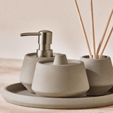 porta sabonete líquido, pote porta algodão e difusor de aromas em cima da bandeja cinza de cimento para banheiro
