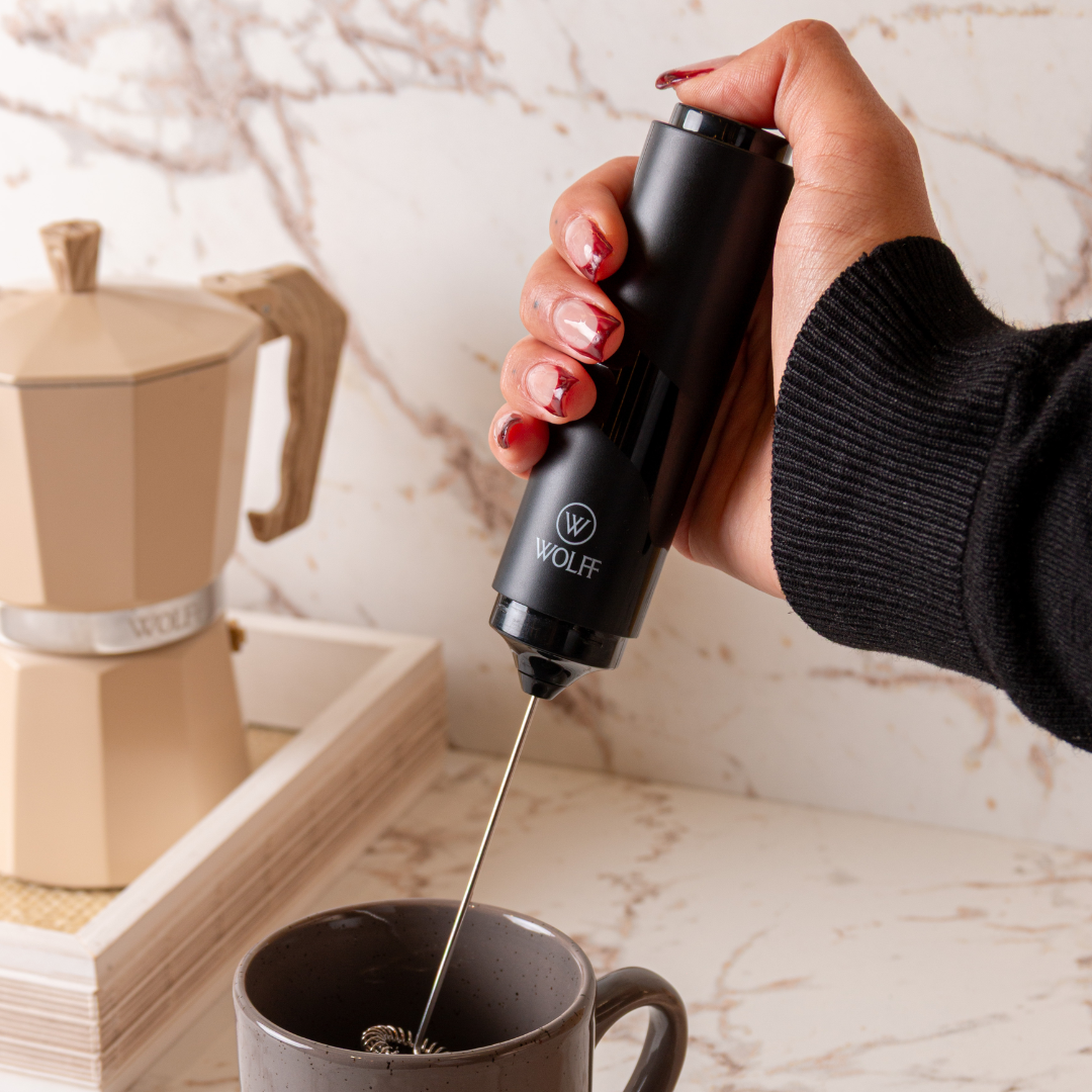mao segurando mini mixer preto sobre xicara de cafe na bancada