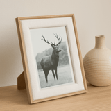porta retrato cervo madeira ao lado de um vaso de cimento bege em cima da bancada de madeira