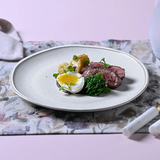Prato raso de cerâmica com ovo frito, carne e vegetais em mesa posta