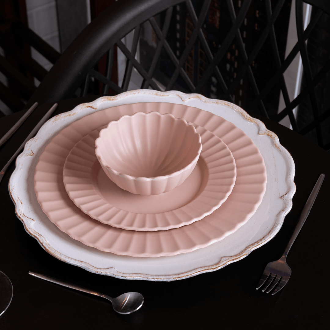 Sousplat branco com acabamento patinado e pratos rosados empilhados na mesa
