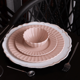 Sousplat branco com acabamento patinado e pratos rosados empilhados na mesa