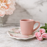 xicara de cafe rosa com pires floral ao lado de rosas sobre bancada de marmore