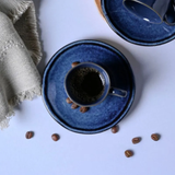 Detalhe da xícara de café com pires azul e grãos espalhados