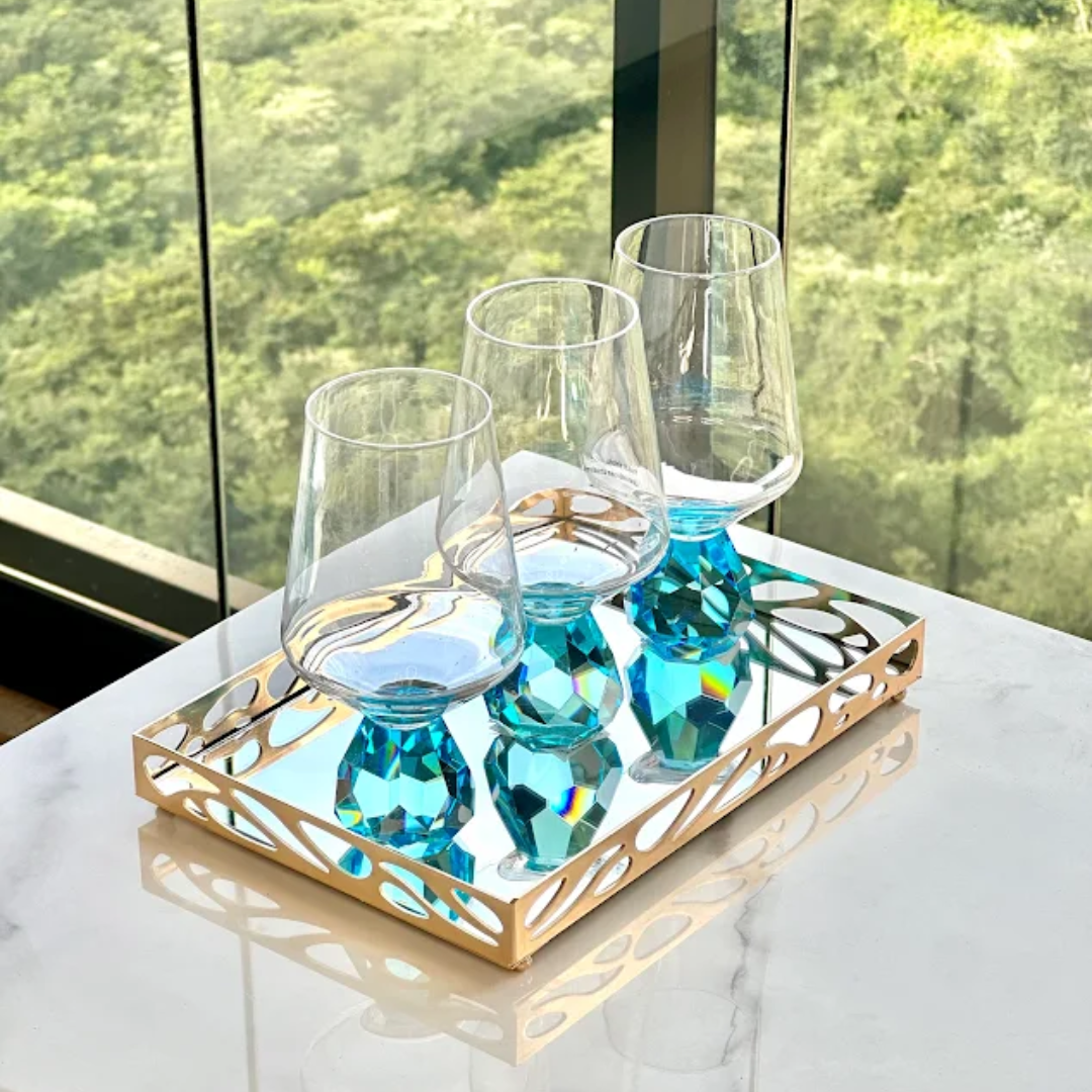 Três taças com base azul em bandeja dourada sobre mesa