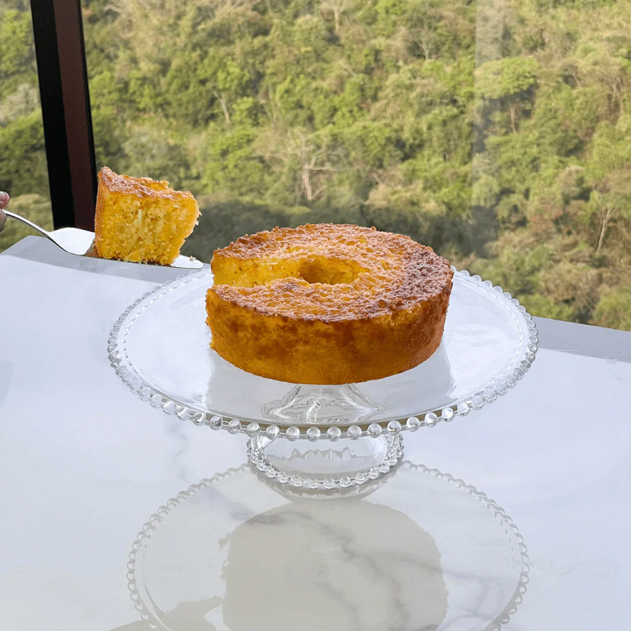 boleira de vidro com bolinhas servindo bolo de cenoura fatiado com vista verde ao fundo