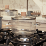 Panela caçarola transparente com alças de metal em fogão aceso