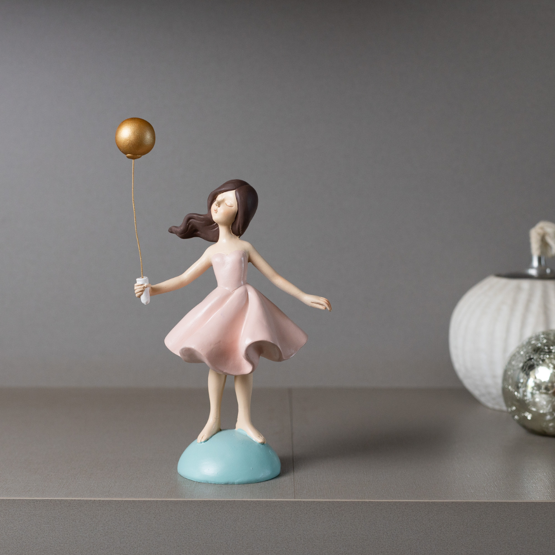 Boneca decorativa com balão dourado em vestido rosa sobre base azul