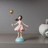 Boneca decorativa com balão dourado em vestido rosa sobre base azul