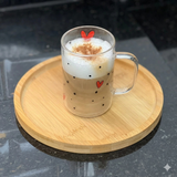Caneca de vidro com café e coração servida em prato de madeira
