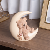 Urso de pelúcia bege sentado em lua de resina decorativa