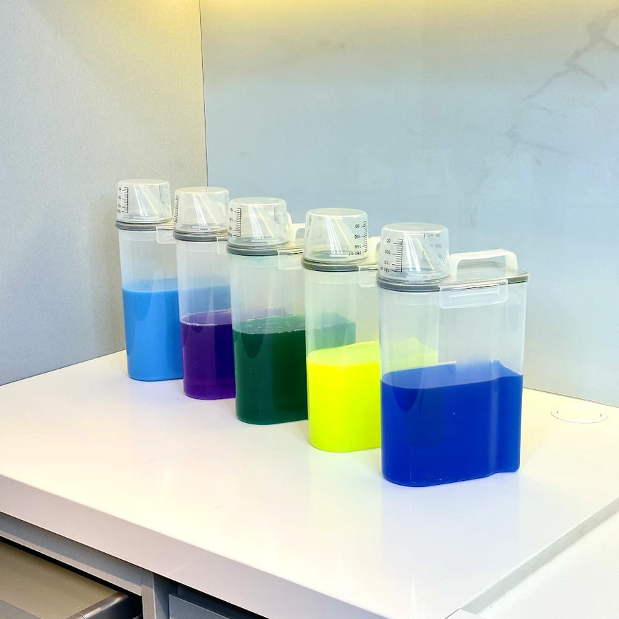 Cinco potes transparentes alinhados com liquidos coloridos sobre bancada branca