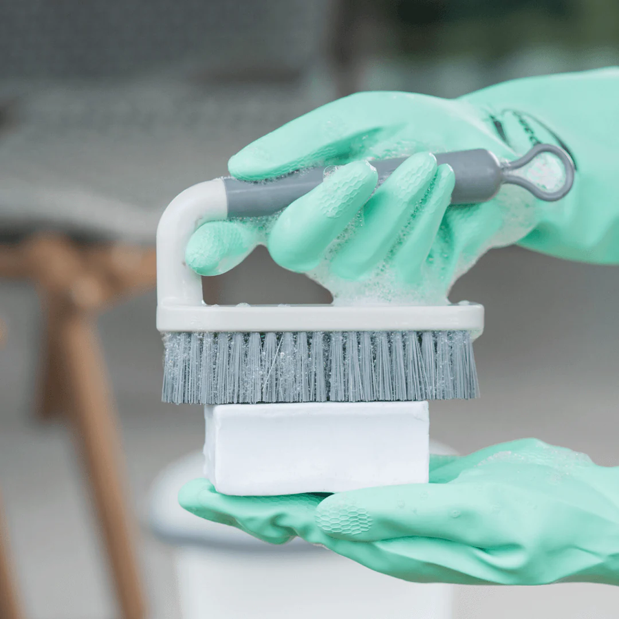 Maos com luvas verdes segurando escova de roupa com sabao