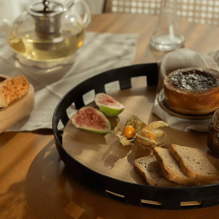 Bandeja redonda preta com figos torradas e cha em mesa de madeira