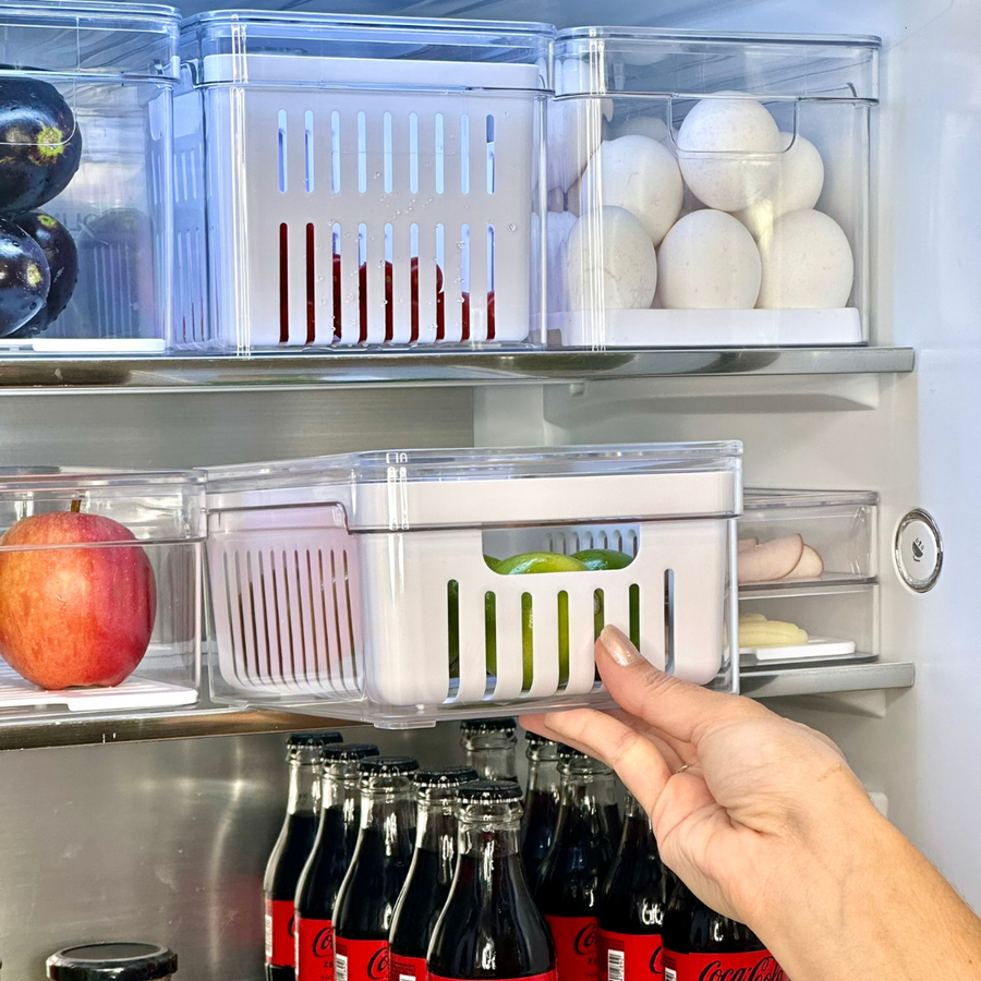 Mão retirando organizador de verduras com furos do compartimento da geladeira