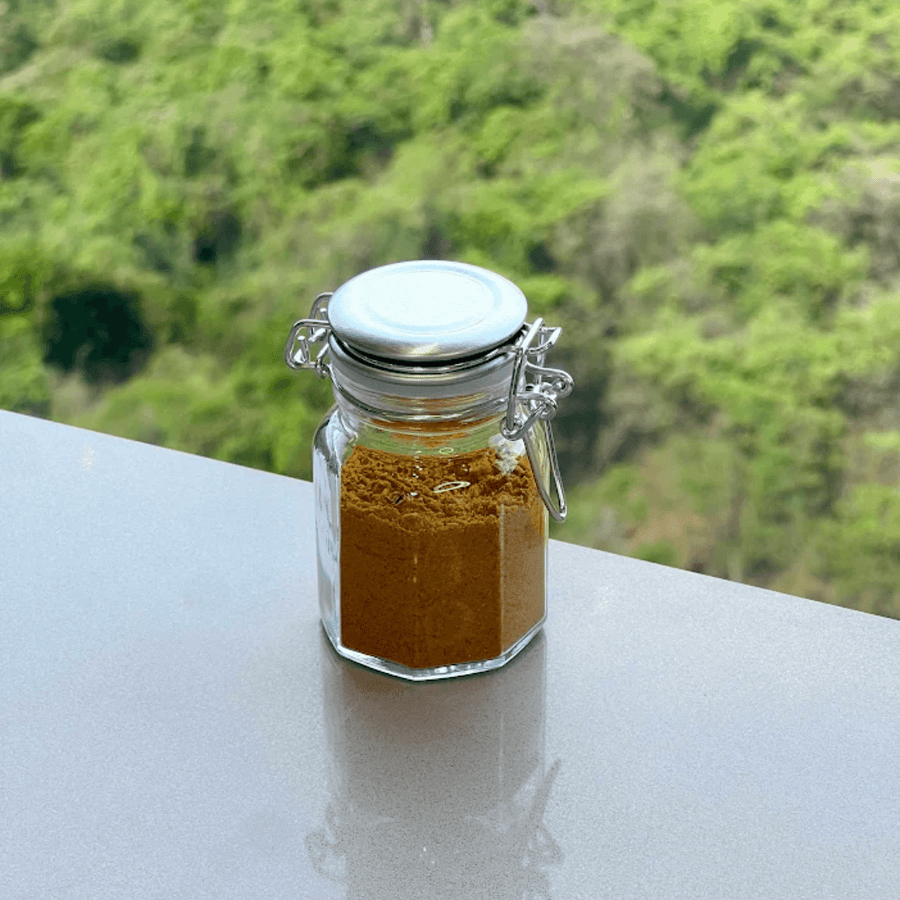 Pote de vidro com tempero em po dourado e fecho de metal cromado em superficie cinza