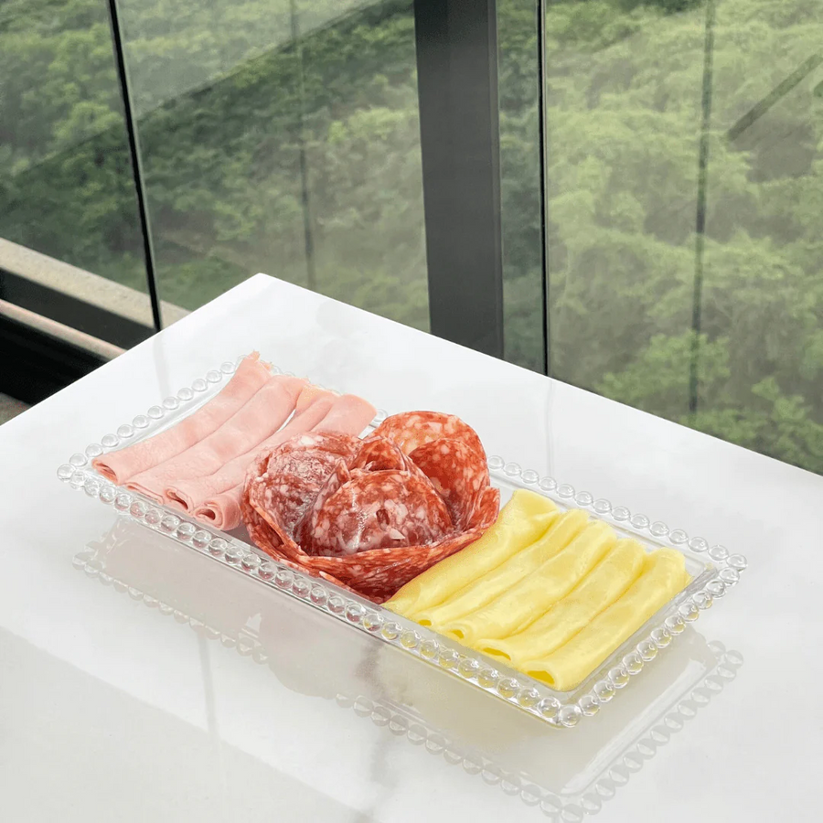 Bandeja retangular de cristal com frios e queijo sobre bancada branca