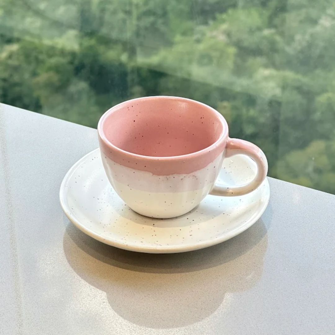 xicara de cafe rosa e branca sobre bancada proxima a janela
