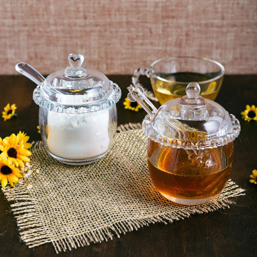Potinhos de cristal com acucar e mel ao lado de xicara de cha e flores amarelas