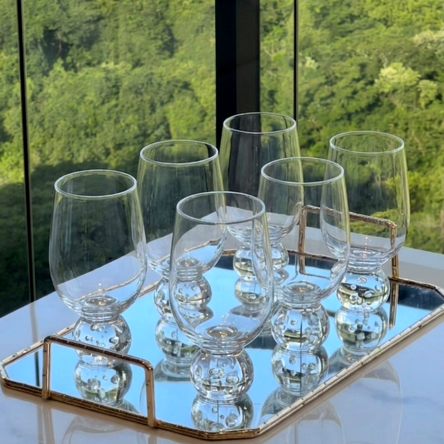 Seis taças para vinho com base esfera em vidro transparente dispostas em bandeja espelhada