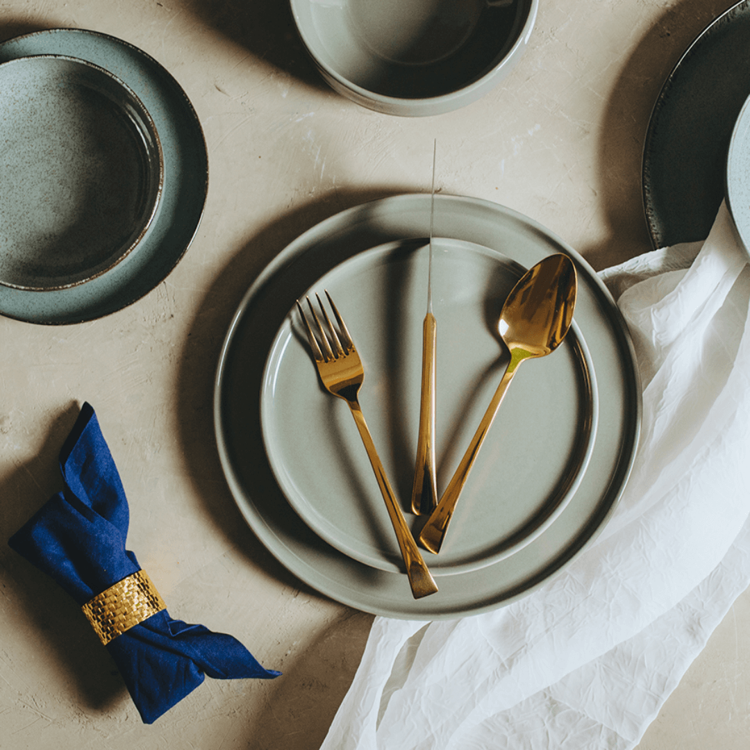 Faqueiro dourado em cima de pratos cinzas na mesa de jantar