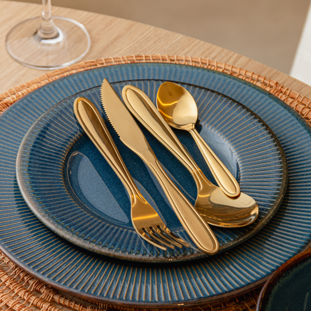 Faqueiro dourado sobre prato azul em mesa posta elegante