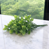 Pick de folhas plásticas verdes flocadas em arranjo natural sobre mármore