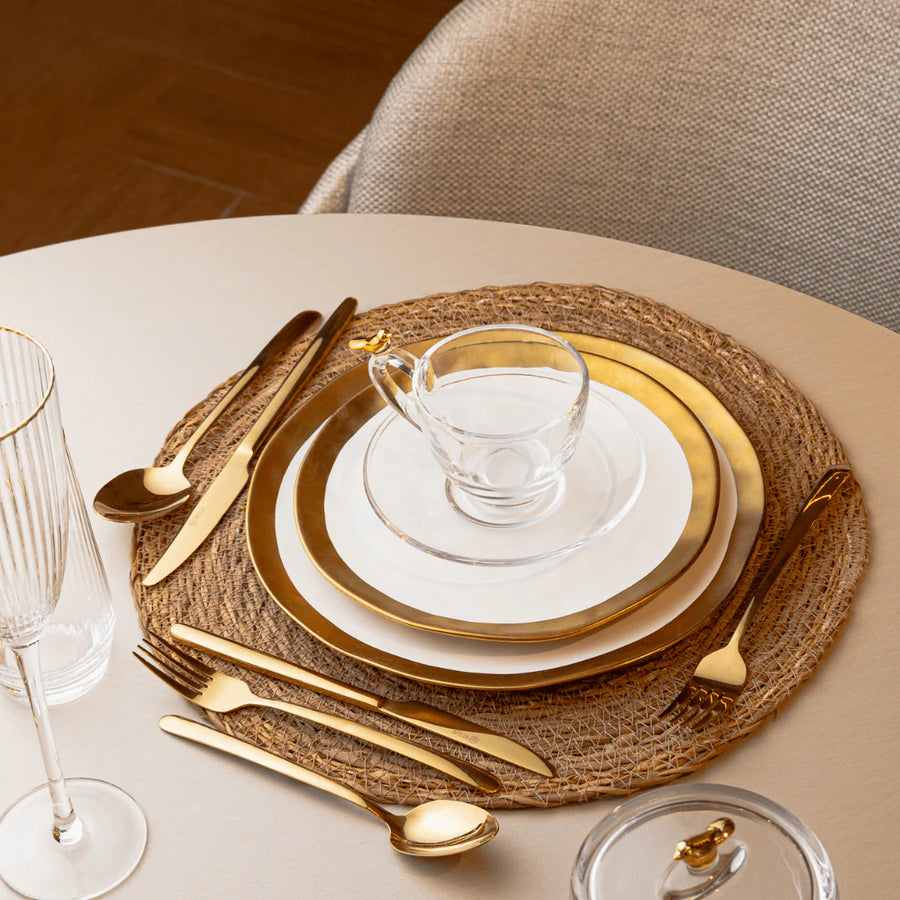 Mesa jantar bege com sousplat palha pratos dourados talheres e tacas de cristal