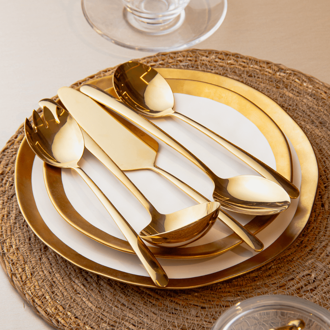pratos com colheres e espátulas douradas na mesa posta com jogo americano dourado