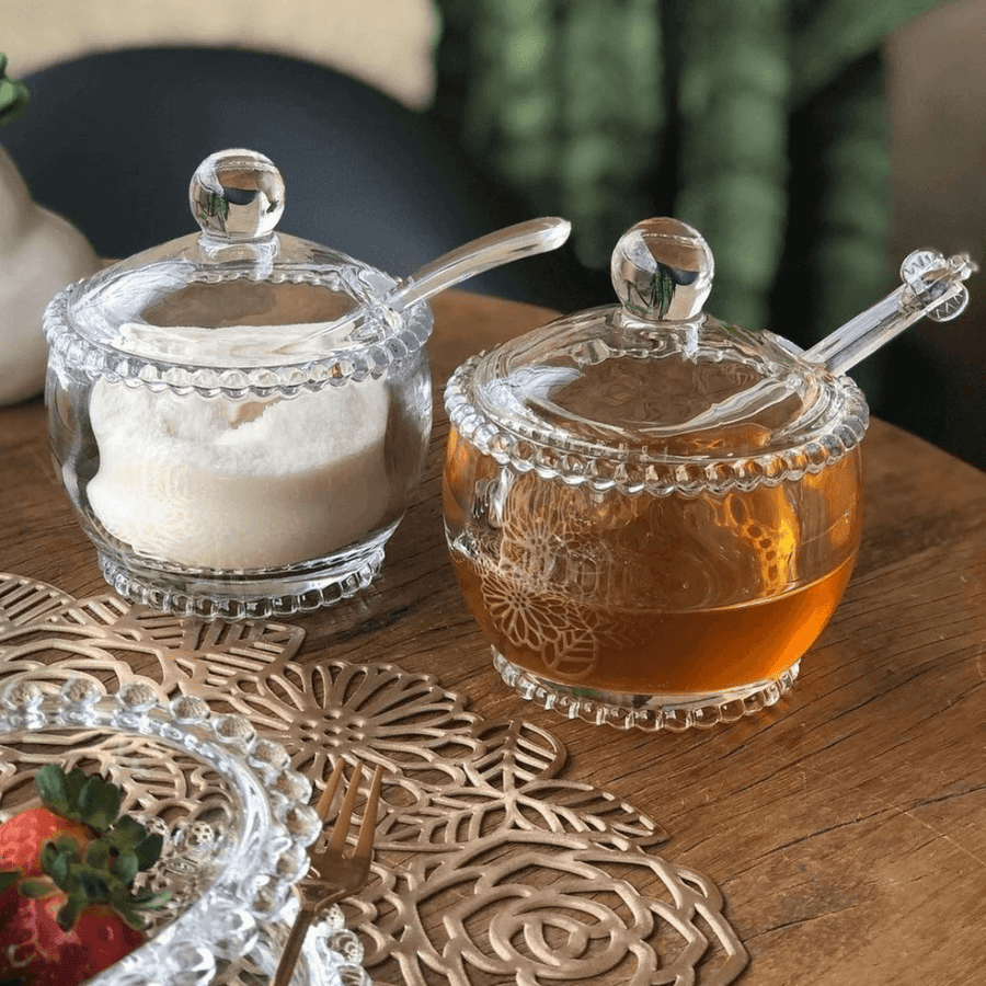 Meleira e açucareiro de cristal com colheres em mesa de madeira