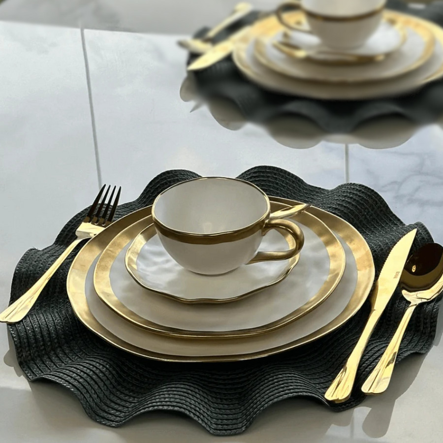 Mesa posta elegante com pratos brancos borda dourada e xicara sobre sousplat preto