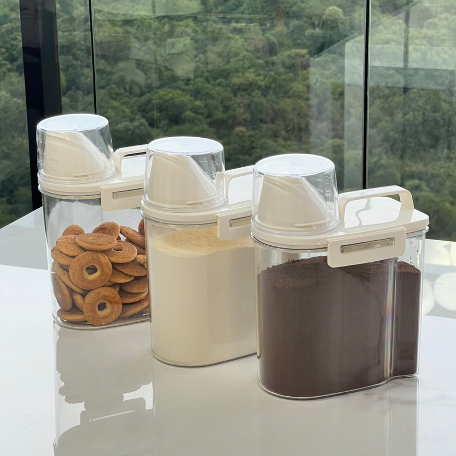 Tres potes hermeticos transparentes com tampas brancas e copos medidores armazenando biscoitos farinha e cafe