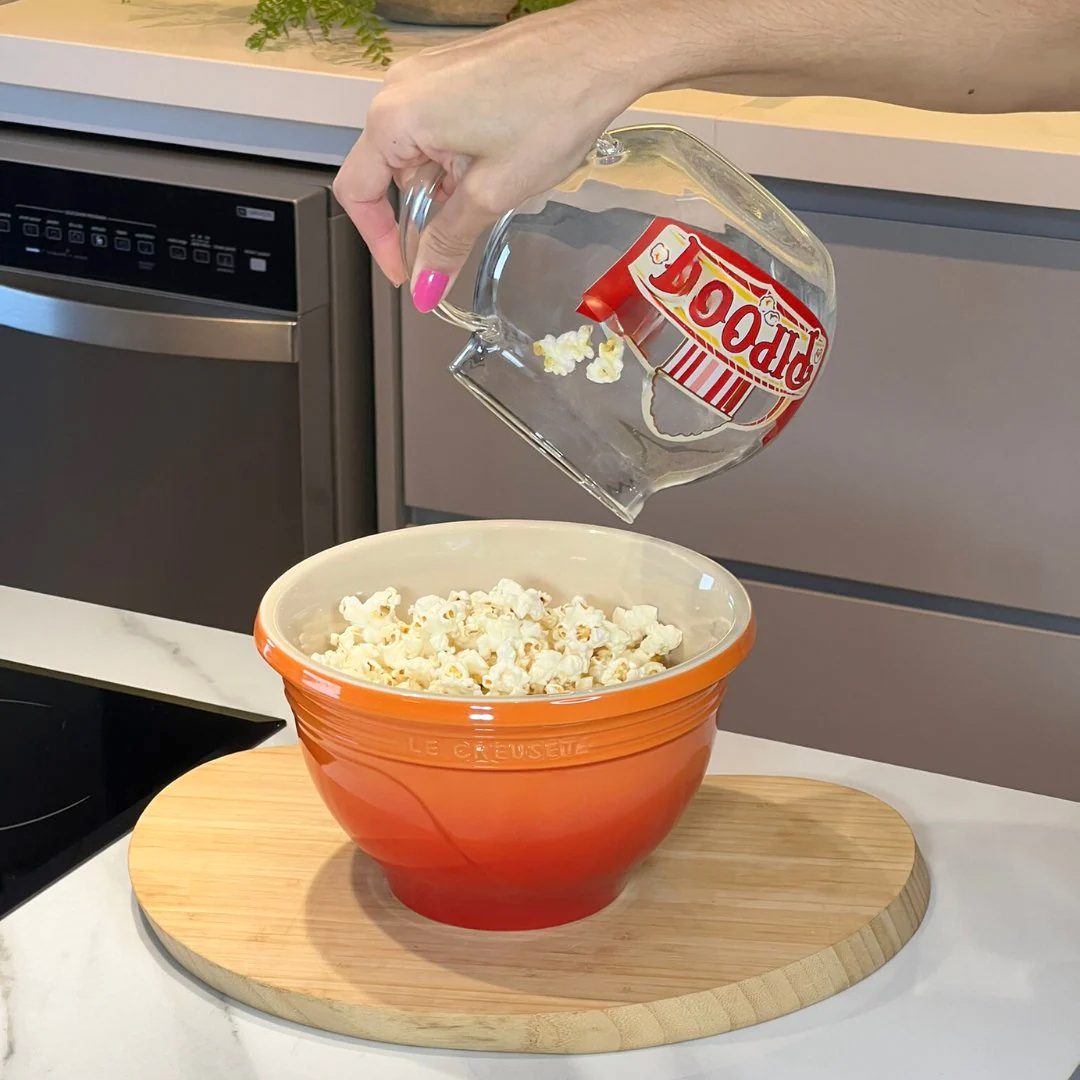 Pipoqueira sendo esvaziada em tigela laranja na cozinha