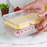 Mãos segurando organizador duplo transparente com queijo fatiado e frios na bancada