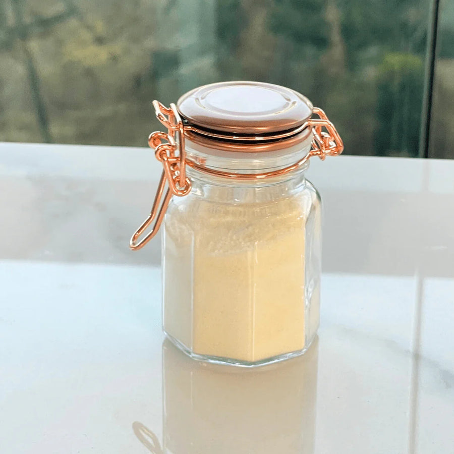 pote de vidro com tempero em po amarelo fechado com trava metalica cobre sobre superficie refletiva