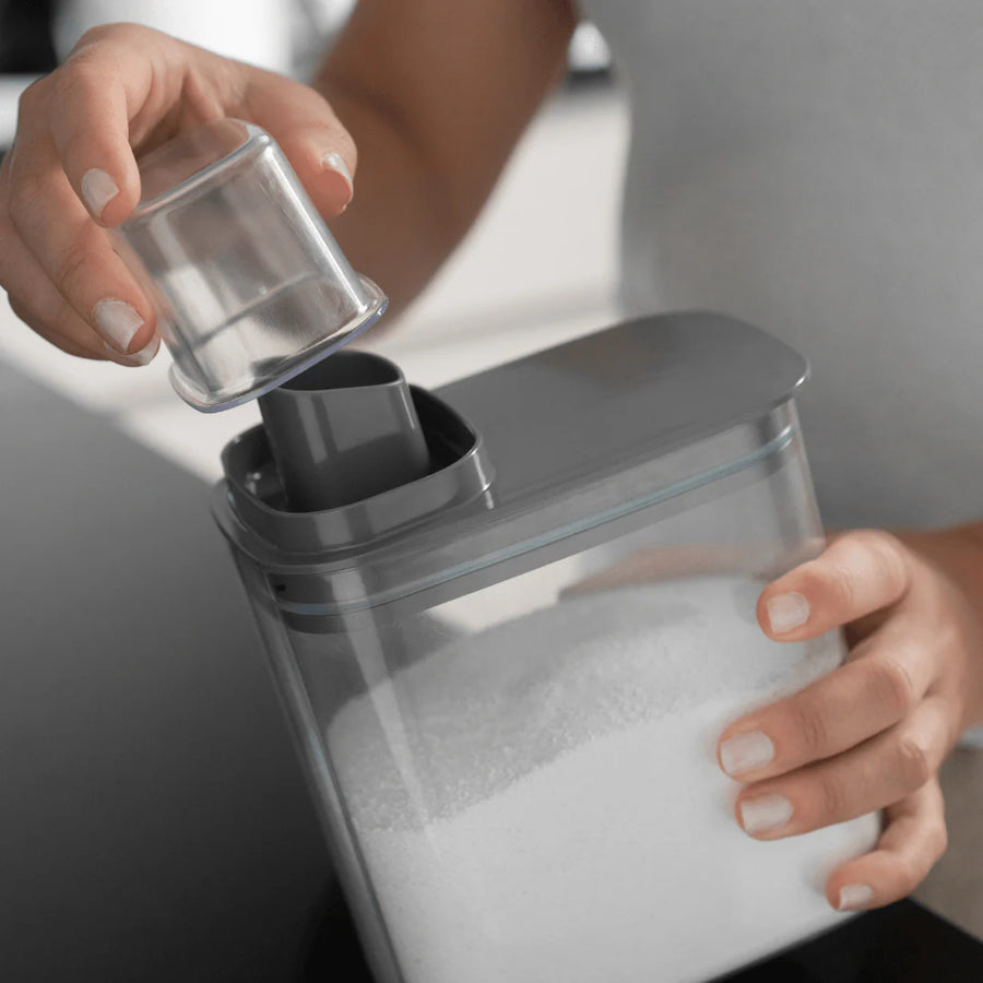 Mãos removendo copo medidor do dispenser organizador de lavanderia