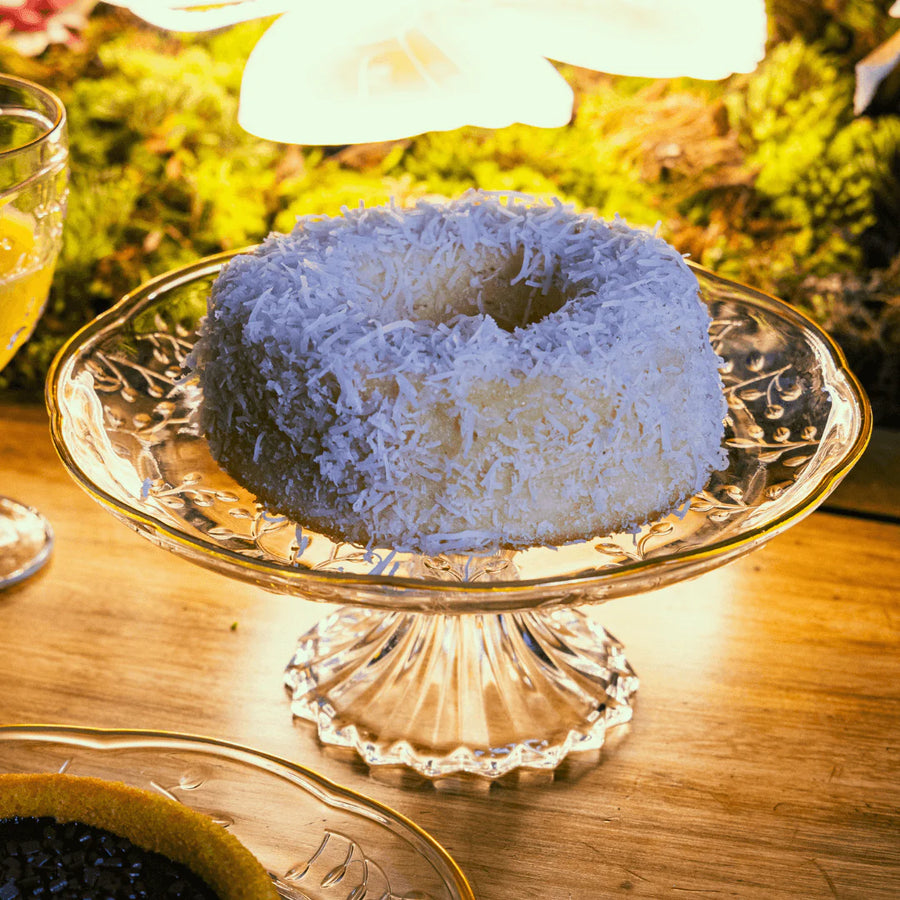 Bolo de coco servido em boloeira de vidro transparente em mesa de cafe da manha