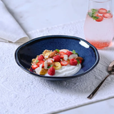 Prato fundo de cerâmica azul com sobremesa de frutas vermelhas e granola na mesa