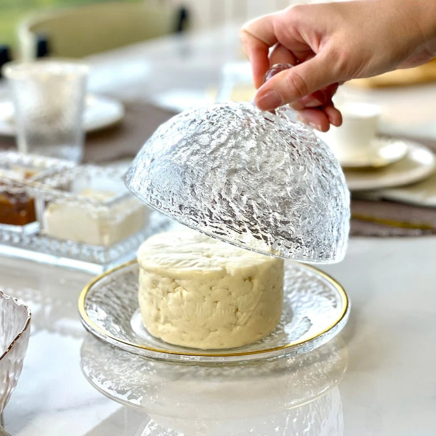 Mao abrindo cloche de cristal martelado revelando queijo fresco em prato