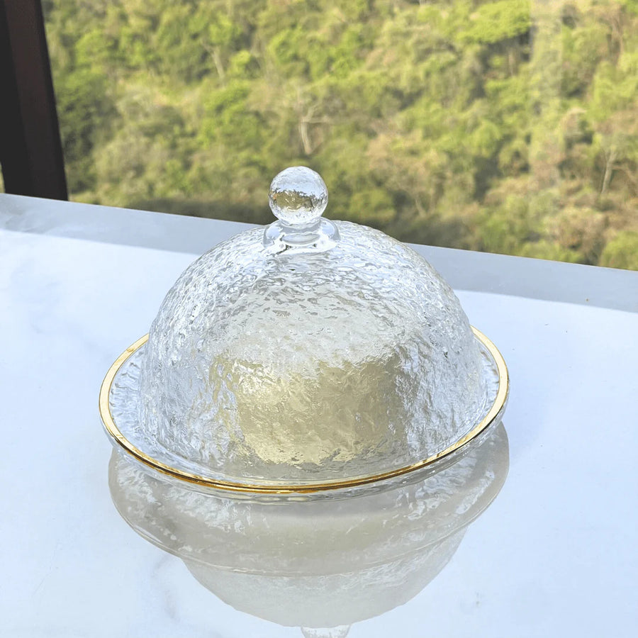 Queijeira de cristal martelado com tampa dome e detalhe dourado sobre mesa de marmore