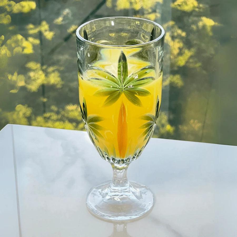 Taca com suco amarelo e estampa tropical iluminada pela luz natural