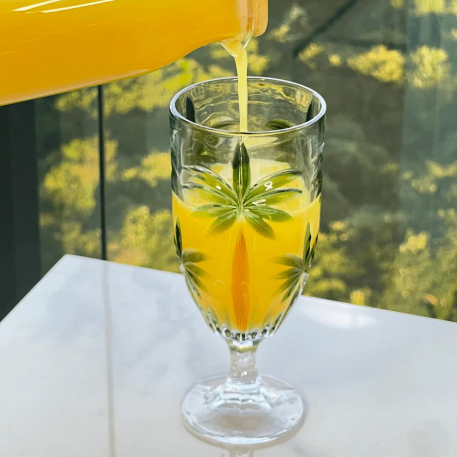 Suco de laranja sendo servido em taca de cristal com desenho de palmeiras