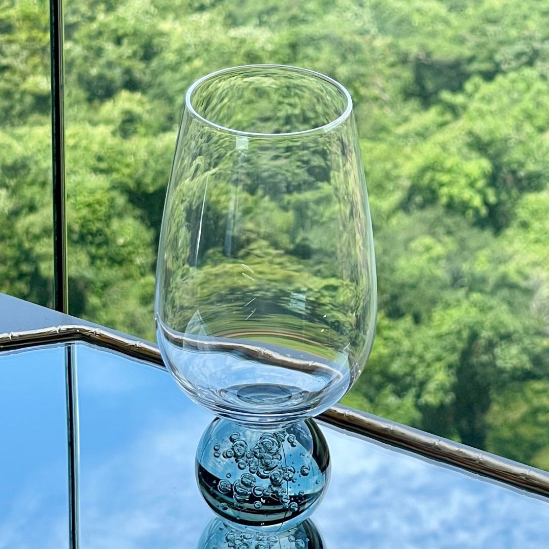 Taca de vidro transparente com base esfera fumê apoiada sobre bandeja espelhada dourada