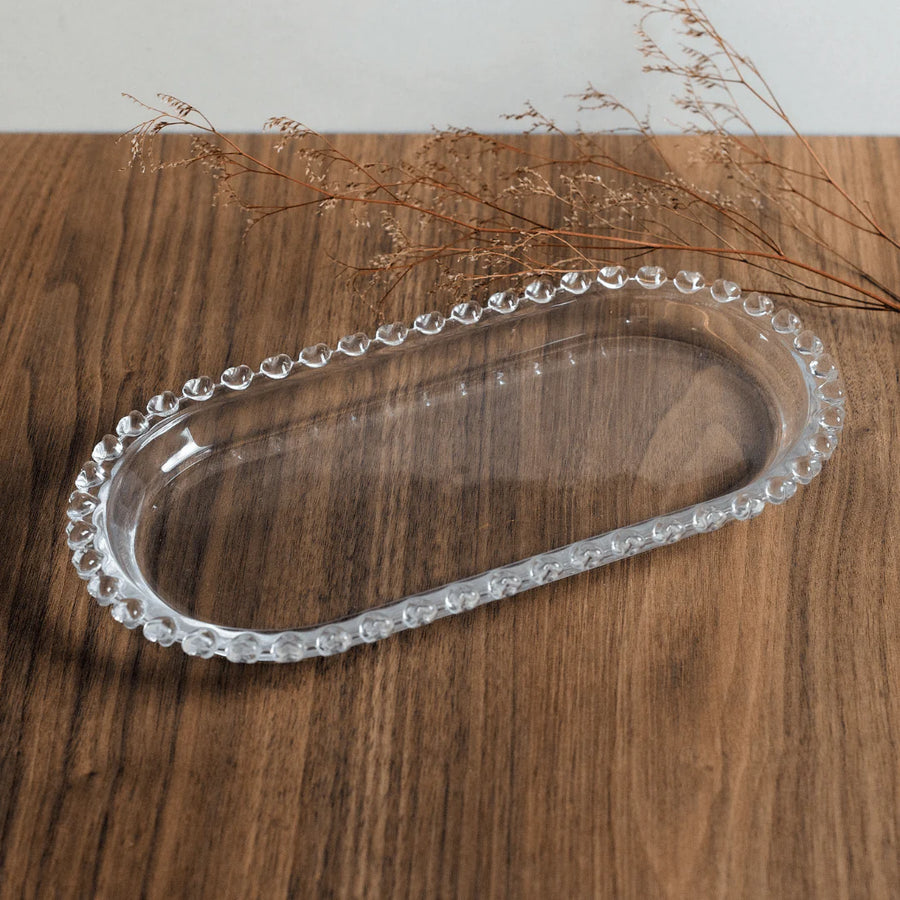 Bandeja oval de cristal com bordas perladas sobre superficie de madeira