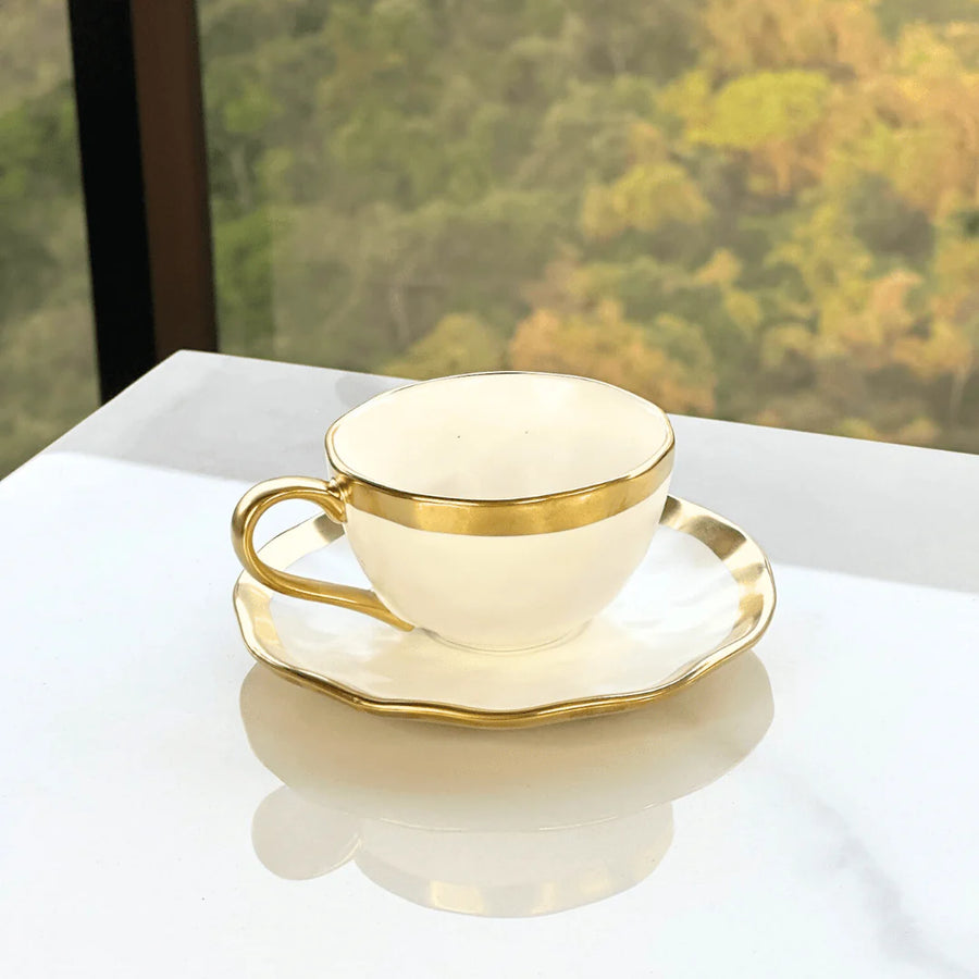 Xicara com pires branco e dourado sobre mesa de marmore com vista para jardim